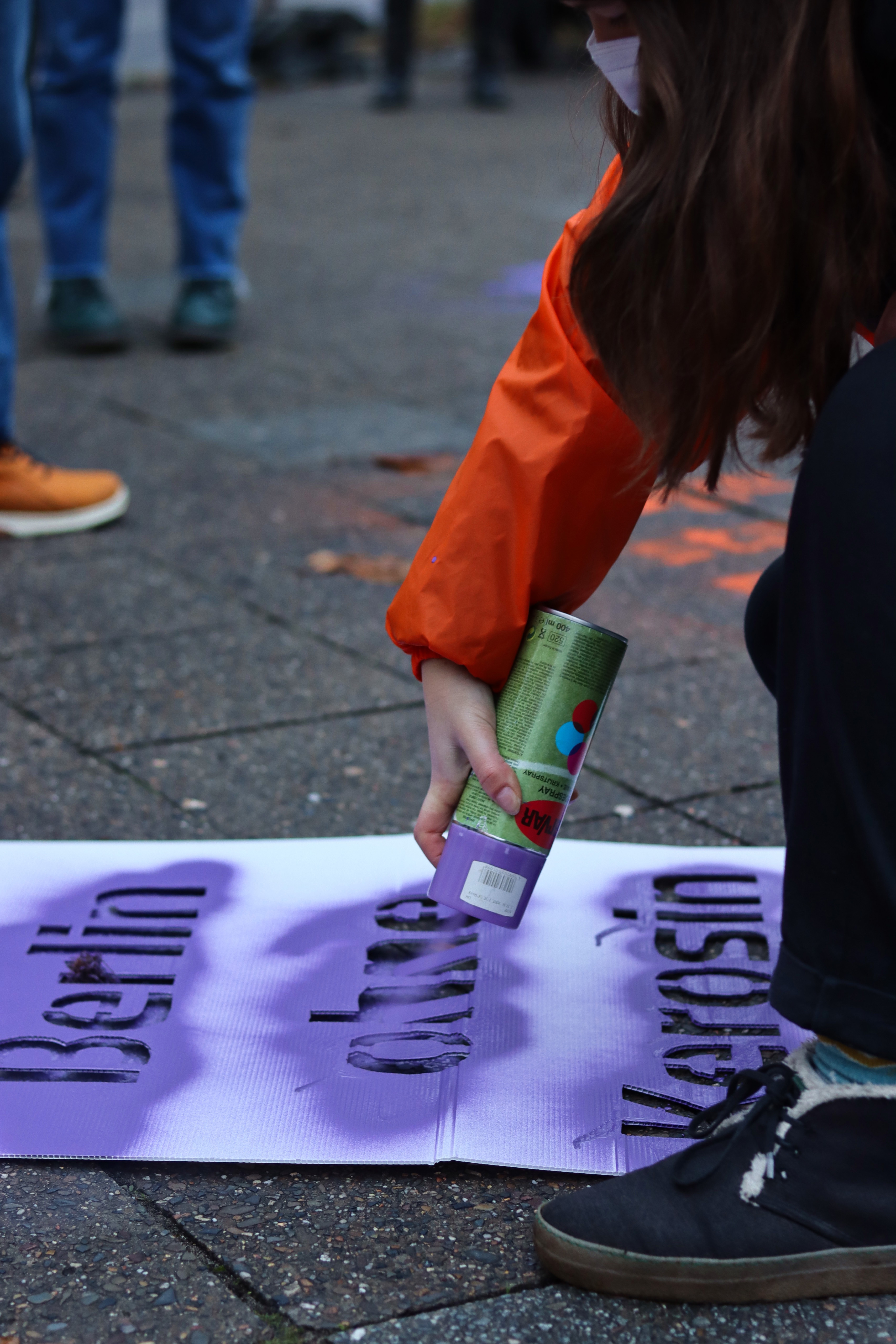 Eine Attac-Aktivistin sprüht Sprühkreide durch eine Schablone auf der "Berlin ohne Kerosin" steht