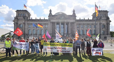Vor dem Reichstagsgebäude stehen mehrere Menschen mit Transparenten und Fahnen und demonstrieren.